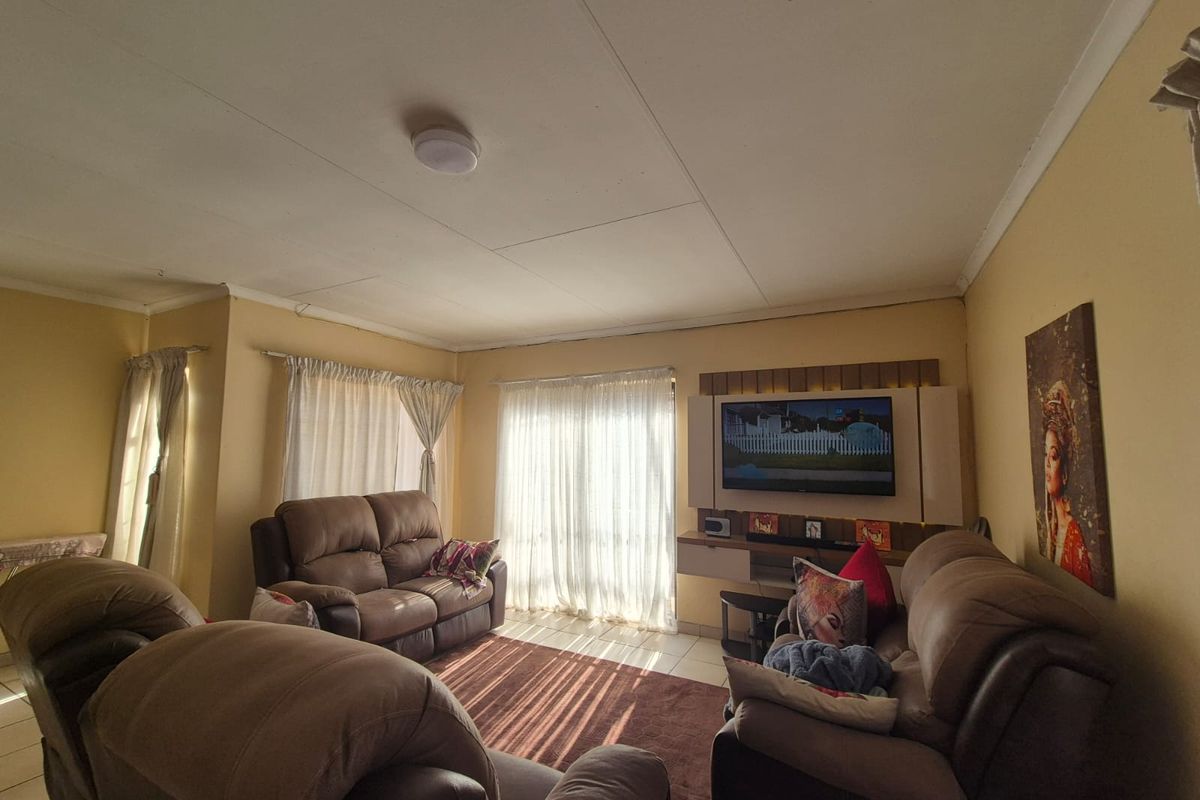 A comfortable living room featuring a built-in media unit, tiled flooring, and natural light through large windows.