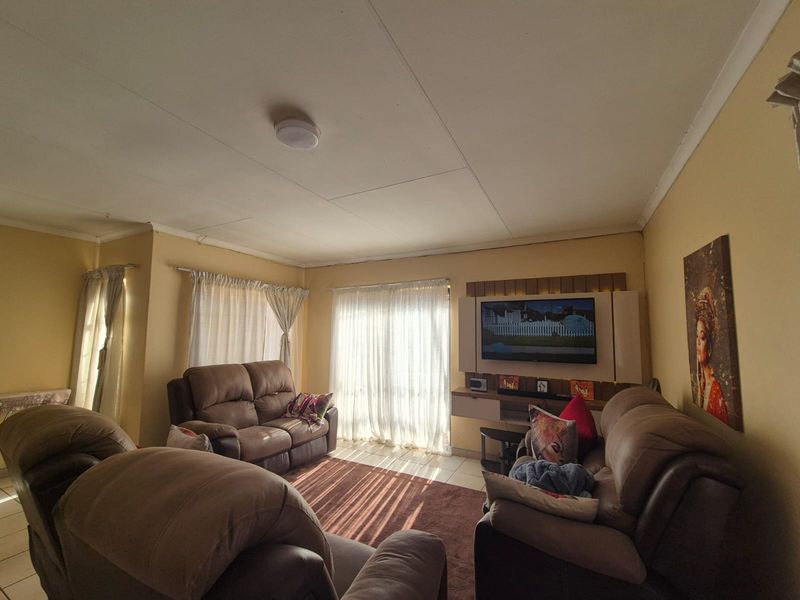 A comfortable living room featuring a built-in media unit, tiled flooring, and natural light through large windows.