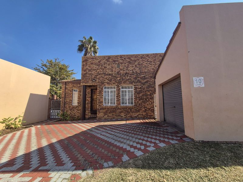 Front exterior view of a face-brick townhouse featuring a paved driveway, single garage, and secure gated entrance.