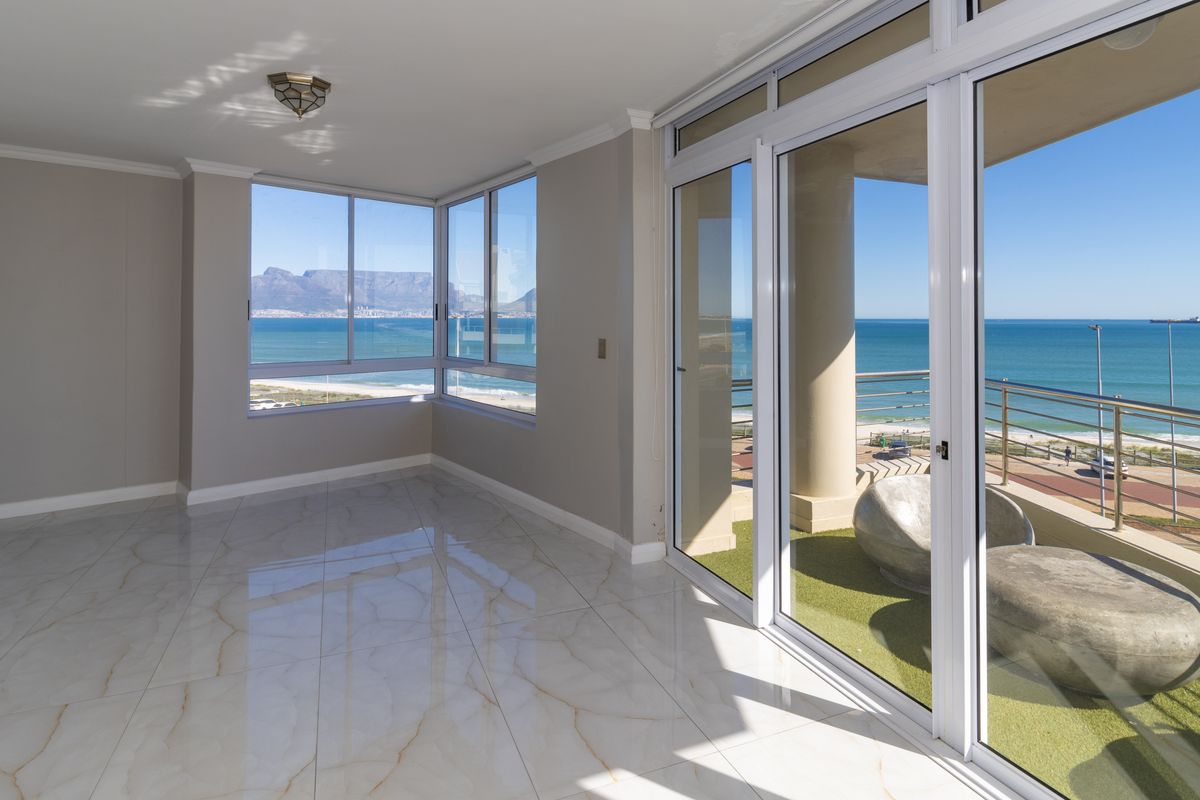 Bright, open-plan living area featuring large-format marble-look tiles, expansive corner windows, and sliding glass doors leading to a balcony with panoramic ocean views.
