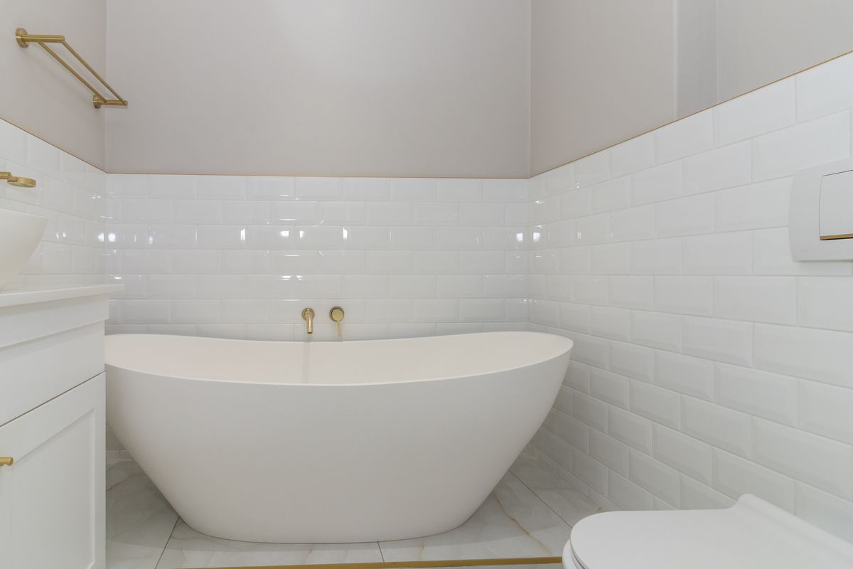 Modern bathroom featuring a sleek freestanding bathtub, wall-mounted basin, and elegant brass fixtures set against clean white subway tiling.