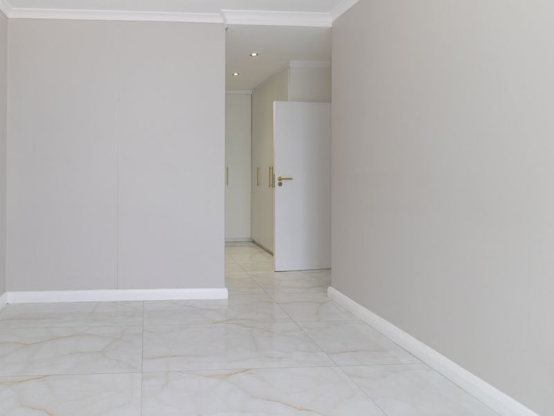A bright, empty bedroom featuring neutral walls, modern marble-look tiled flooring, and built-in storage cupboards with a clean, minimalist aesthetic.