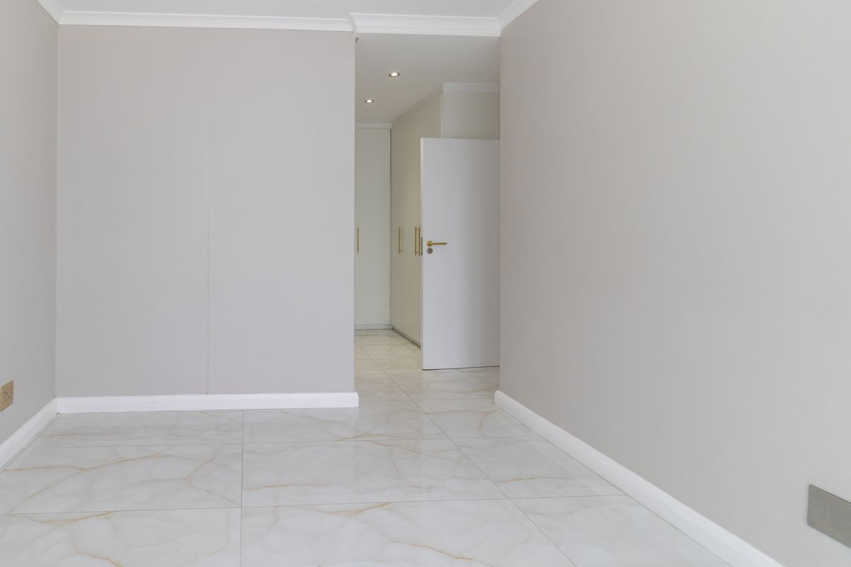 A bright, empty bedroom featuring neutral walls, modern marble-look tiled flooring, and built-in storage cupboards with a clean, minimalist aesthetic.