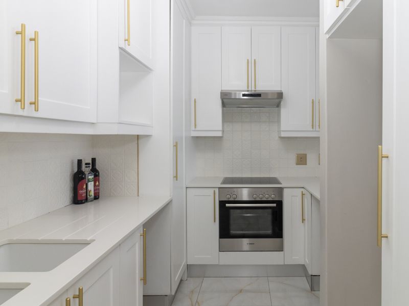 Modern, well-appointed kitchen featuring white shaker-style cabinetry, gold hardware, integrated appliances, and elegant marble-look floor tiles.
