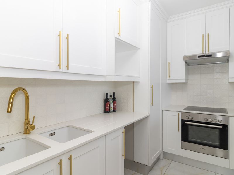 Modern kitchen featuring white shaker-style cabinetry, brass hardware, stone countertops, integrated stainless steel appliances, and a stylish textured tile backsplash.