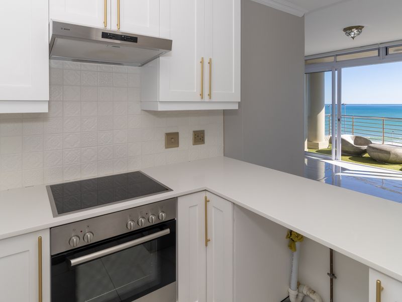 Modern kitchen featuring white cabinetry, quartz countertops, and integrated appliances, with an open-plan layout leading to a balcony with ocean views.