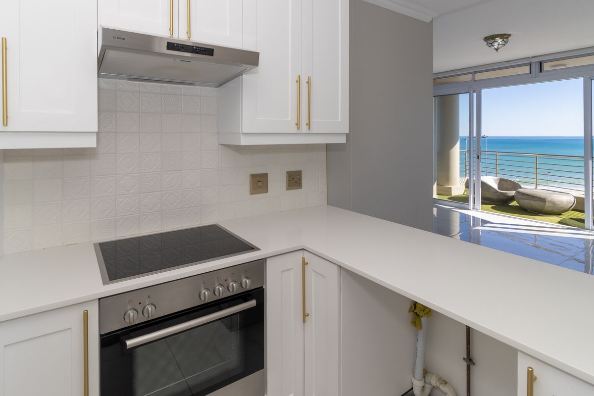 Modern kitchen featuring white cabinetry, quartz countertops, and integrated appliances, with an open-plan layout leading to a balcony with ocean views.