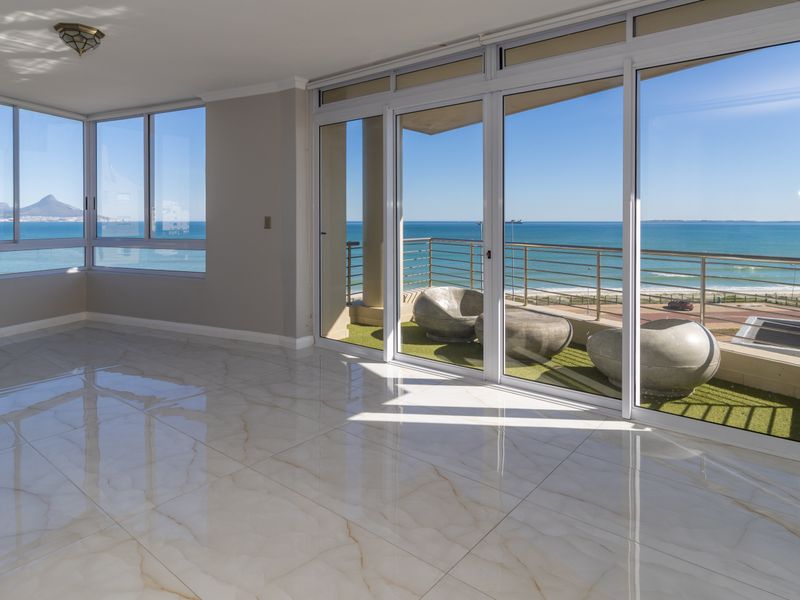 Spacious, light-filled living area featuring polished marble-look floor tiles and expansive sliding glass doors opening onto a balcony with panoramic ocean views.