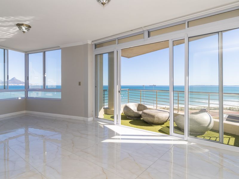 Bright and spacious living area featuring polished marble-look floor tiles and large sliding glass doors opening onto a balcony with stunning ocean views.