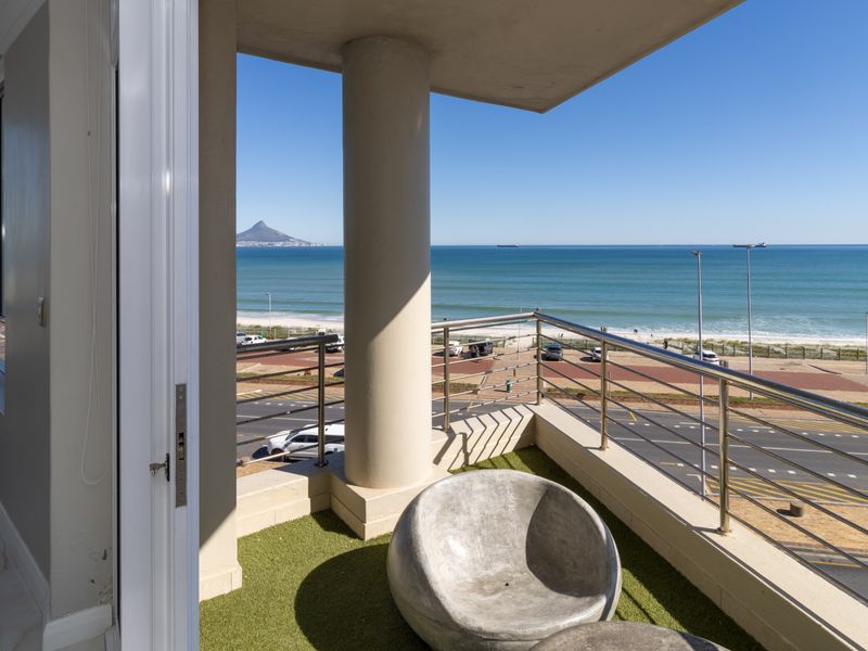 A spacious balcony featuring stainless steel railings and a concrete column, offering panoramic ocean and coastal views.