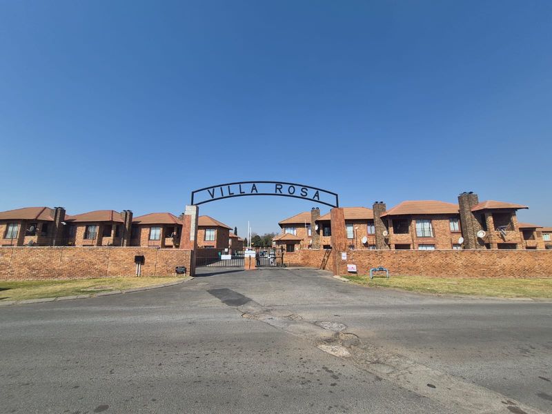 Front entrance view of the Villa Rosa townhouse complex, featuring brick construction, tiled roofing, and a secure gated access point.