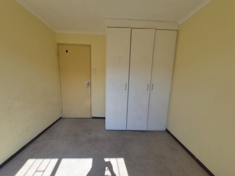 An empty bedroom featuring built-in wardrobes, carpet flooring, and neutral wall finishes, offering a blank canvas for potential updates and modernization.