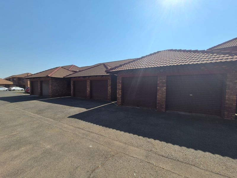 Exterior view of a townhouse complex featuring multiple brick garages with tiled roofs and a paved driveway area.