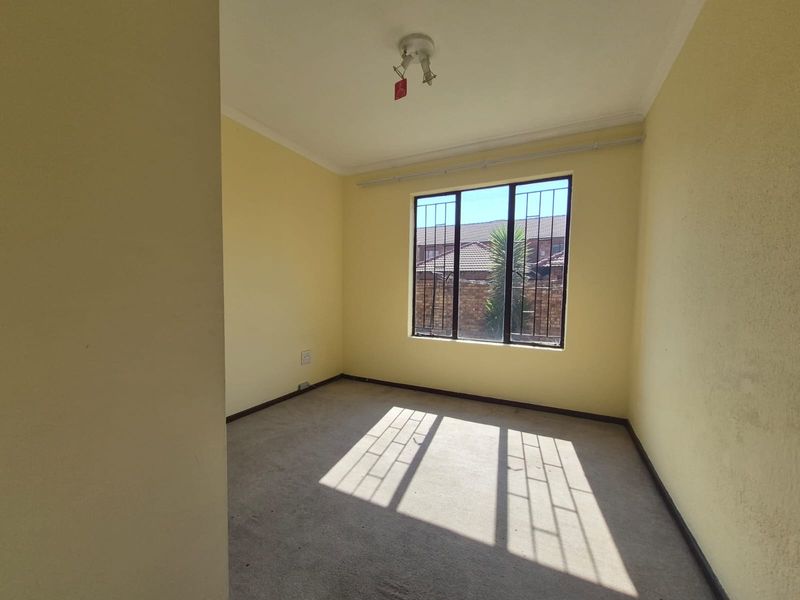 An empty bedroom featuring carpet flooring, yellow walls, and a window fitted with security bars.