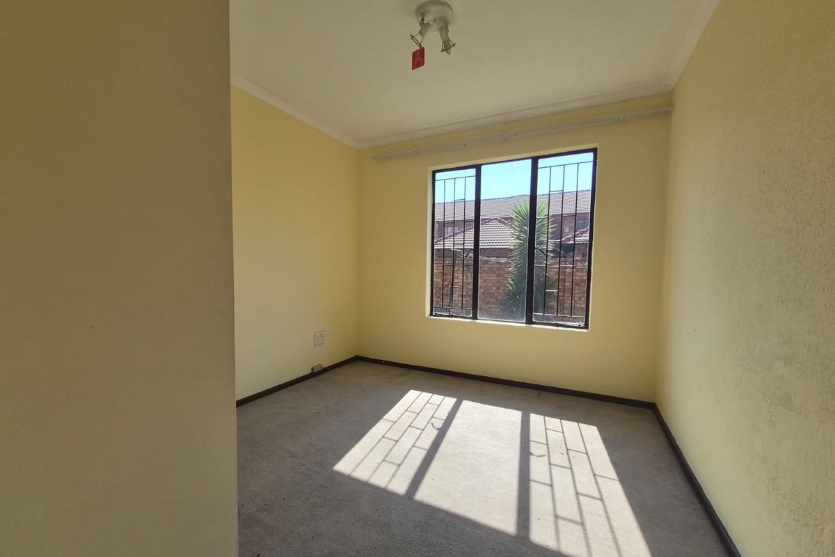 An empty bedroom featuring carpet flooring, yellow walls, and a window fitted with security bars.