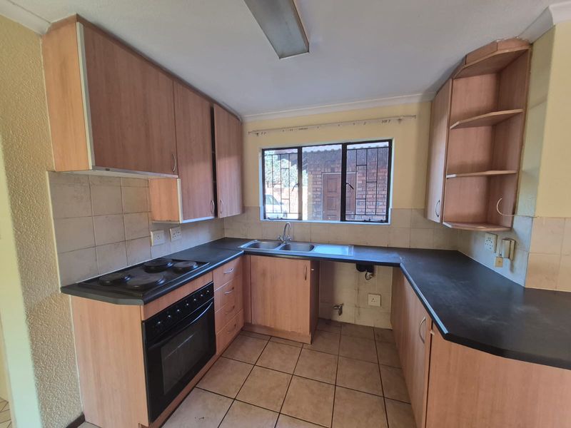 A functional kitchen featuring built-in wooden cabinetry, dark laminate countertops, an integrated electric oven and hob, and tiled flooring.