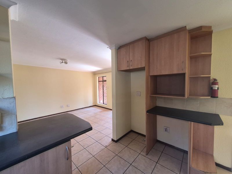 Open-plan living and kitchen area featuring tiled flooring, built-in wooden cabinetry, and security bars on the windows.