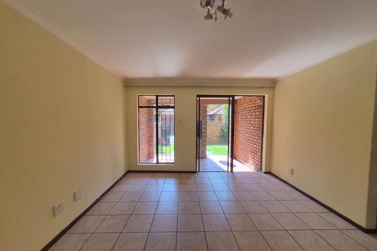 An empty living room featuring ceramic floor tiles, coving, and a sliding glass door providing access to an outdoor patio area.
