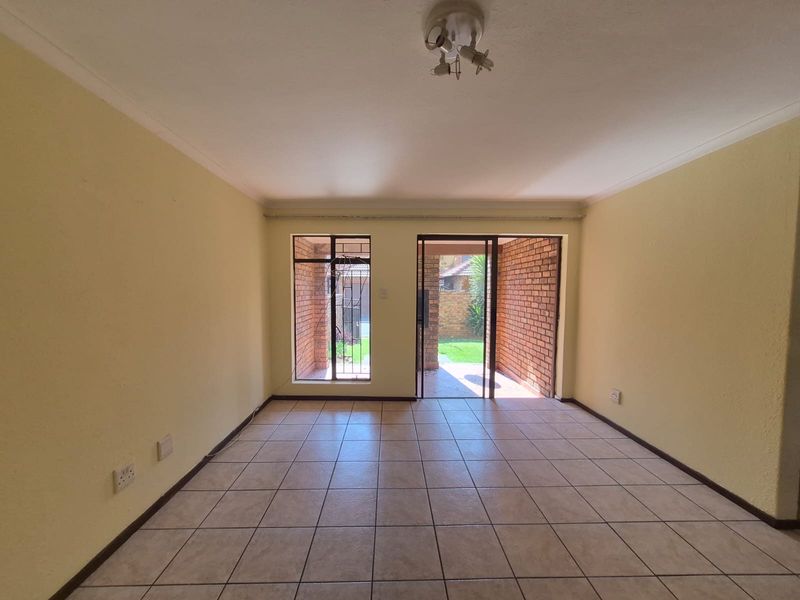 An empty living room featuring ceramic floor tiles, coving, and a sliding glass door providing access to an outdoor patio area.