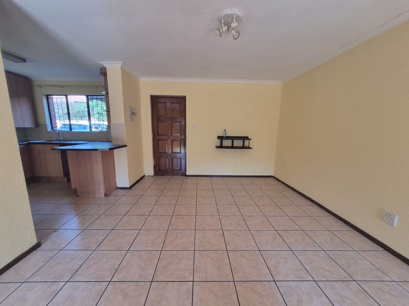 An open-plan living and kitchen area featuring tiled flooring, wooden cabinetry, and a neutral color palette, offering a functional and versatile living space.