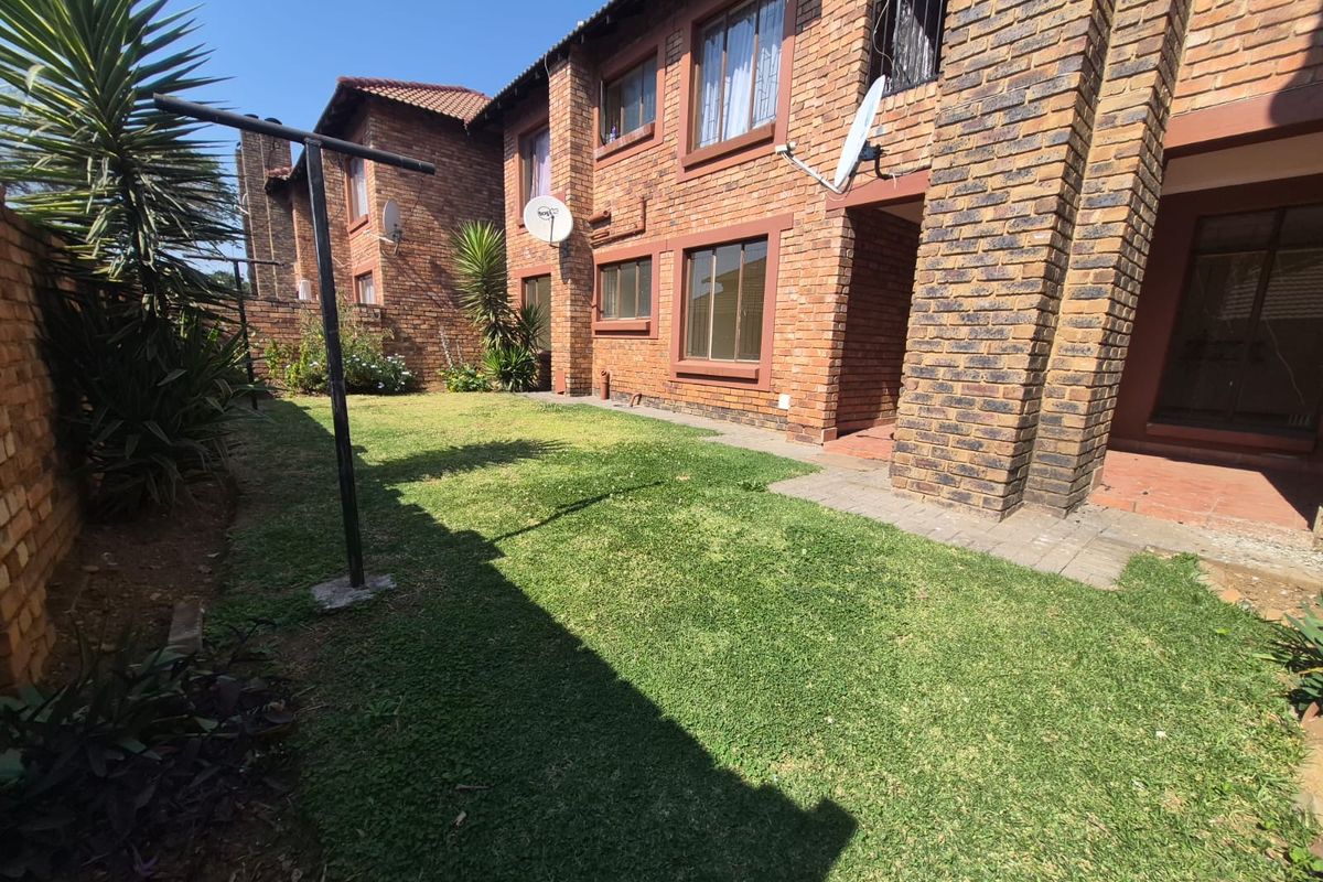 A rear view of a face brick townhouse featuring a private garden area with a lawn and paved walkway.