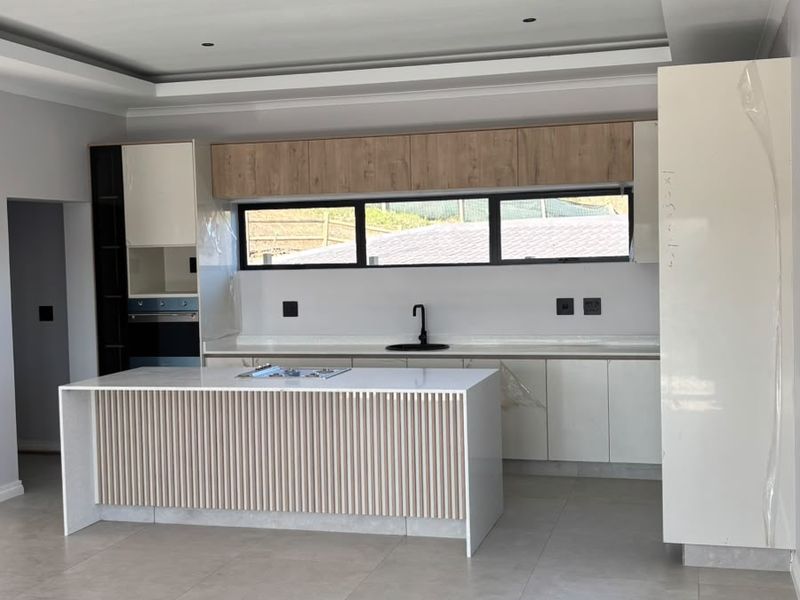 Modern, newly installed kitchen featuring a central island with slatted detailing, sleek cabinetry, built-in appliances, and neutral floor tiles in an open-plan layout.