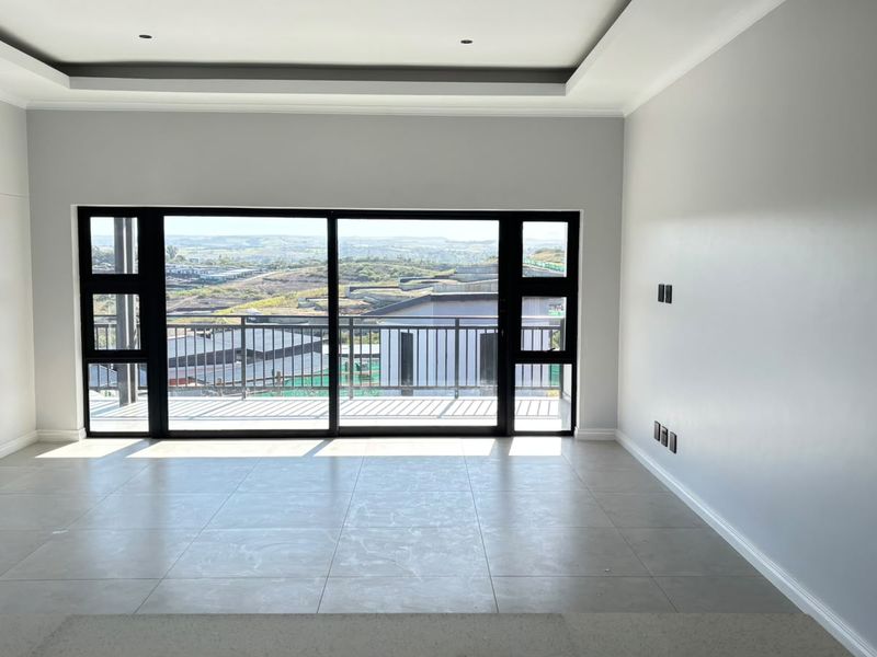 A bright, empty living room featuring modern tiled floors, recessed ceiling lighting, and large sliding glass doors opening to a balcony with scenic views.