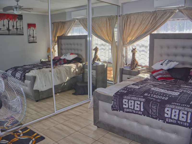 A bedroom featuring tiled flooring, a ceiling fan, a wall-mounted air conditioning unit, and large mirrored sliding wardrobe doors.