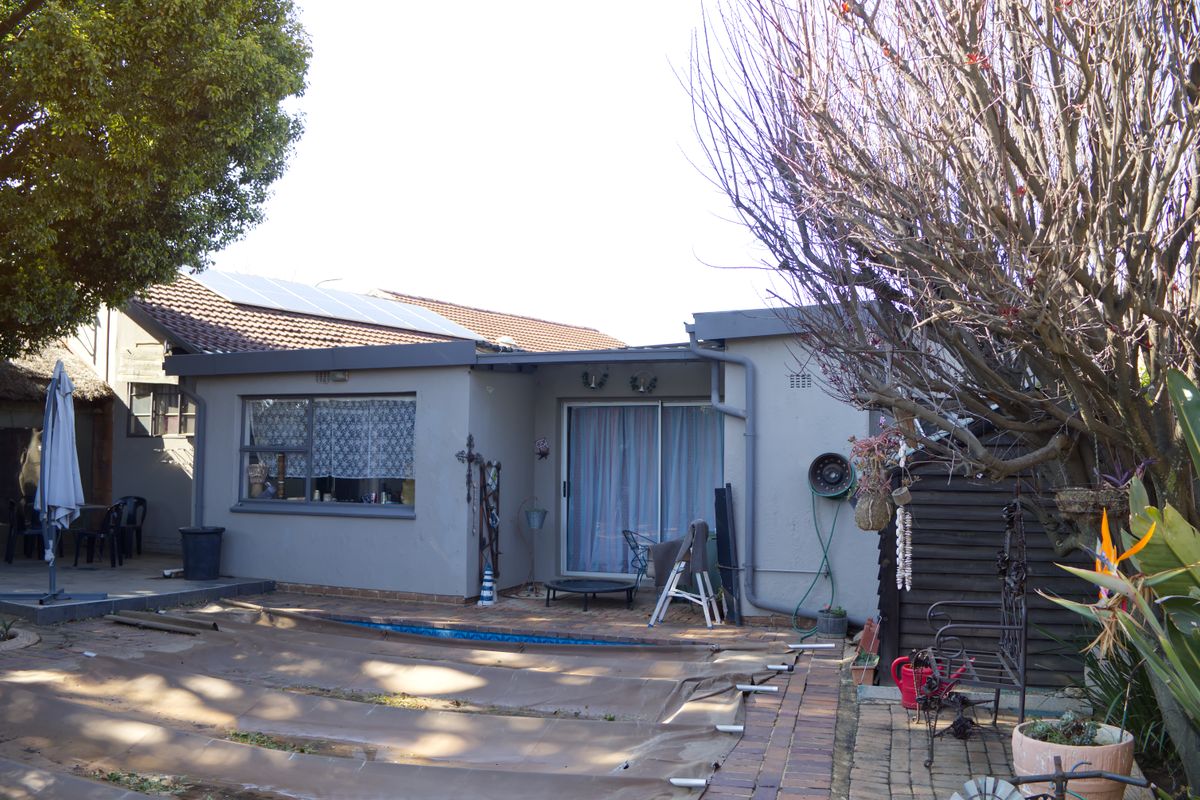 Rear view of the property featuring a paved patio area, swimming pool with cover, and solar panels installed on the tiled roof.
