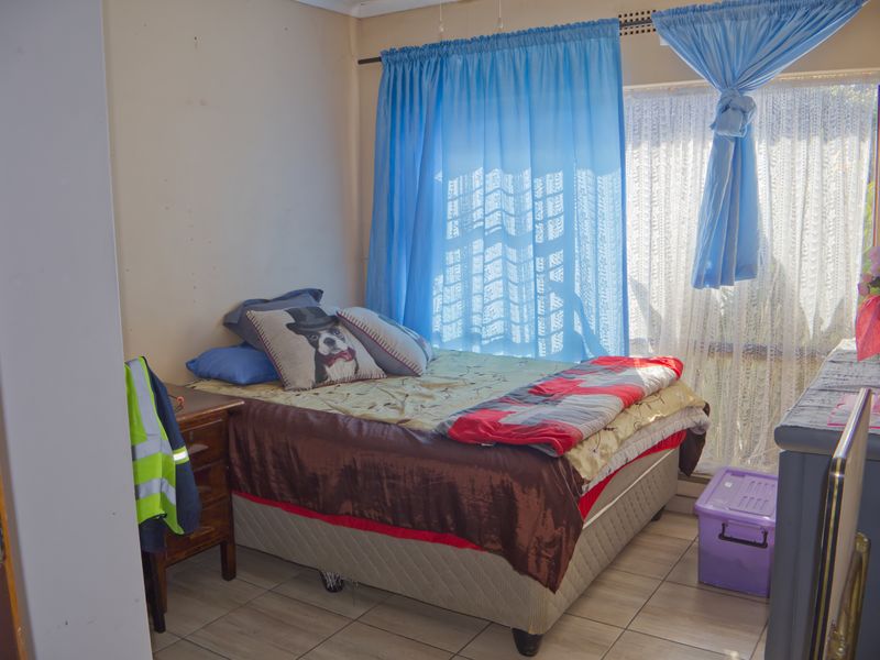 A bedroom featuring tiled flooring and natural light through a window with curtain rails.