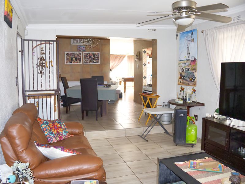 Open plan living and dining area featuring tiled flooring, ceiling fan, and a raised dining section with access to adjacent rooms.
