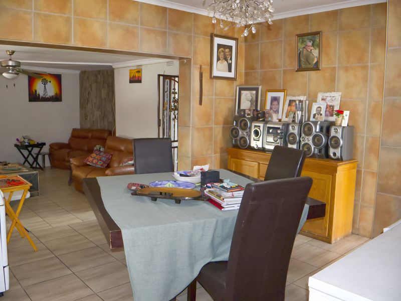 Open plan dining and living area featuring ceramic wall tiling, tiled flooring, and a ceiling fan, providing a functional and connected living space.