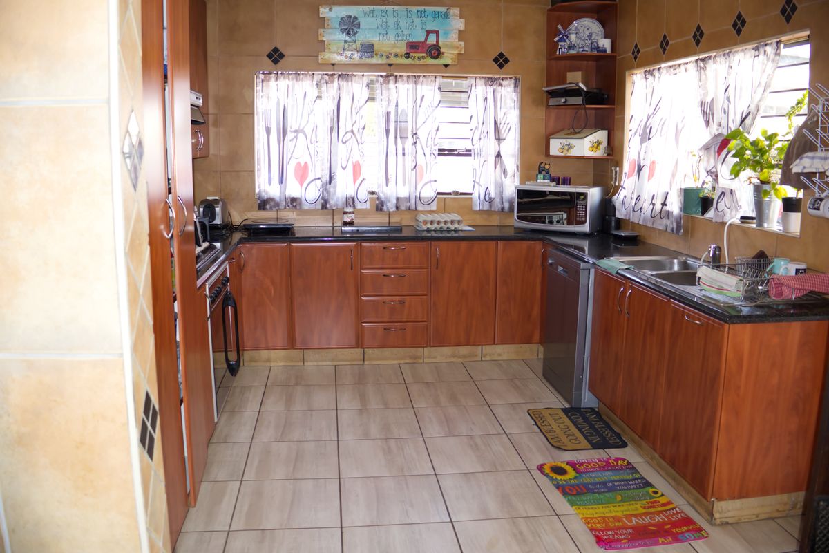 A functional kitchen featuring wood-look laminate cabinetry, granite countertops, and a double bowl stainless steel sink with tiled flooring and walls.