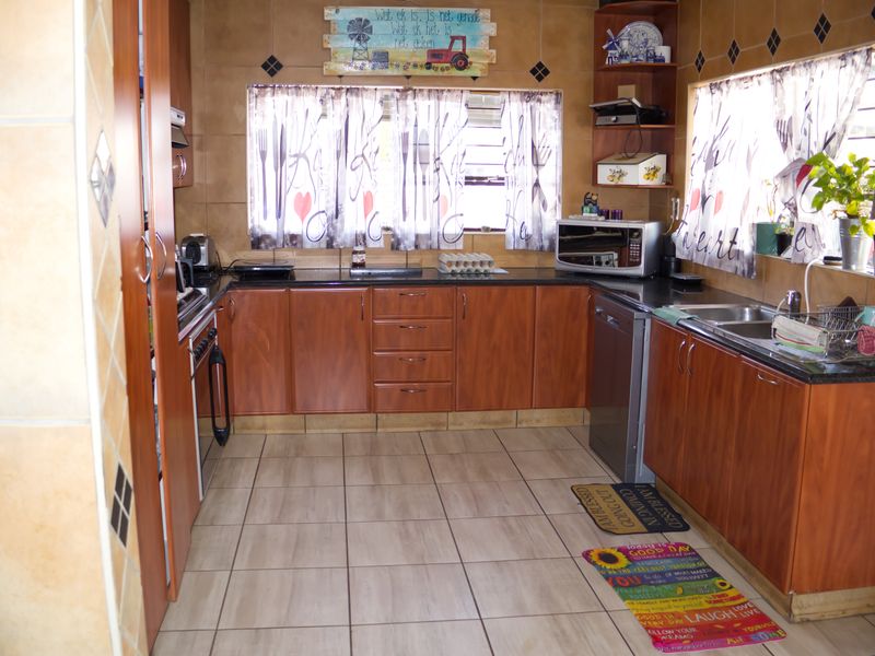 A functional kitchen featuring wood-look laminate cabinetry, granite countertops, and a double bowl stainless steel sink with tiled flooring and walls.