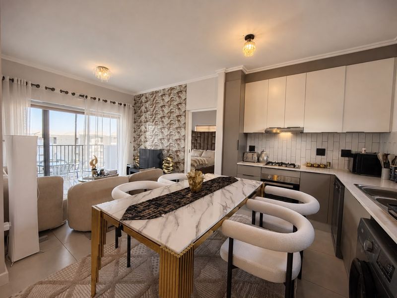 Modern open-plan apartment featuring a sleek kitchen with built-in appliances, dining area, and seamless flow to a private balcony through sliding glass doors.
