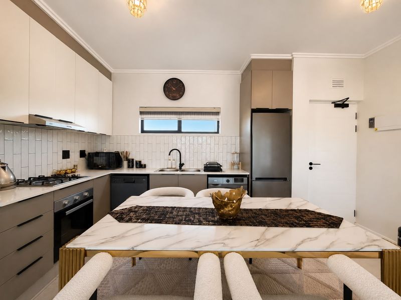 Modern open-plan kitchen featuring sleek two-tone cabinetry, stone countertops, subway tile backsplash, and integrated appliances, seamlessly flowing into the dining area.