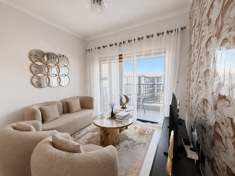 A well-lit living room featuring tiled flooring, a decorative feature wall, and a sliding glass door providing access to a private balcony.