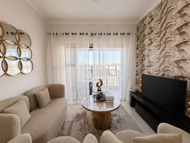 A well-maintained living room featuring a large sliding glass door leading to a balcony, complemented by a decorative textured feature wall.