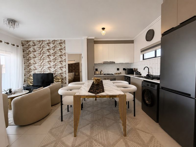 Modern open-plan living and kitchen area featuring sleek cabinetry, subway tile backsplash, integrated appliances, and tiled flooring in a well-maintained apartment setting.