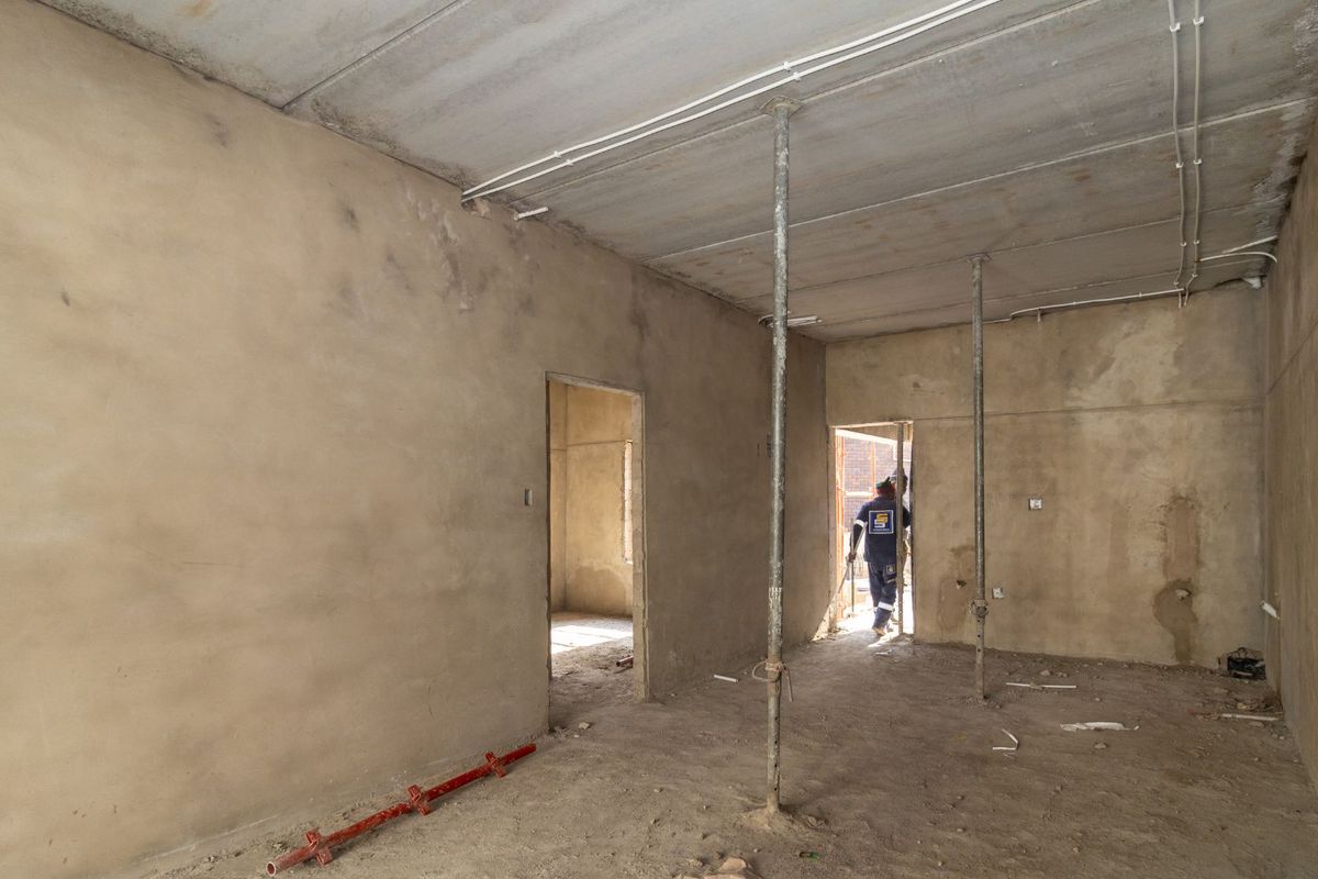 An unfinished interior space currently under construction, featuring exposed concrete ceilings, plastered walls, and temporary structural support props.