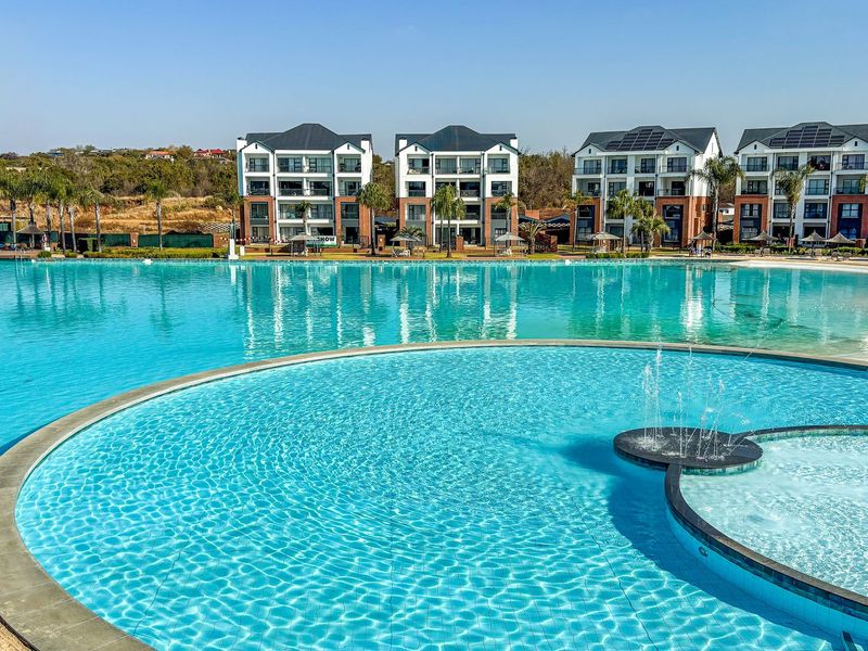 A large, well-maintained communal swimming pool with a water feature, set against a backdrop of modern multi-story apartment buildings.