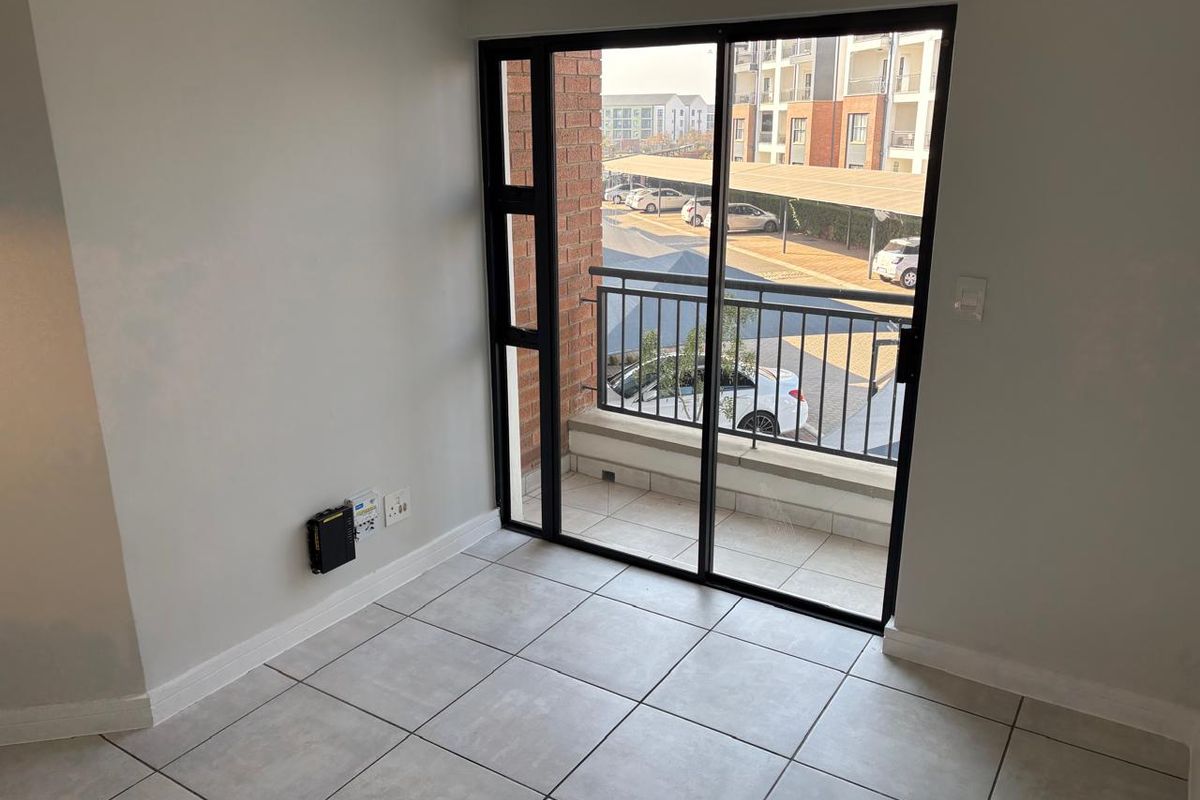 An empty living area featuring neutral tiled flooring and a sliding glass door that opens onto a private balcony with complex views.