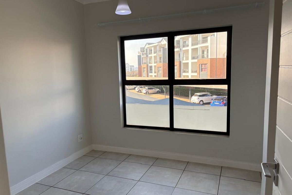 A clean, empty bedroom featuring neutral tiled flooring, modern aluminium window frames, and a simple pendant light fixture, ready for personalization.
