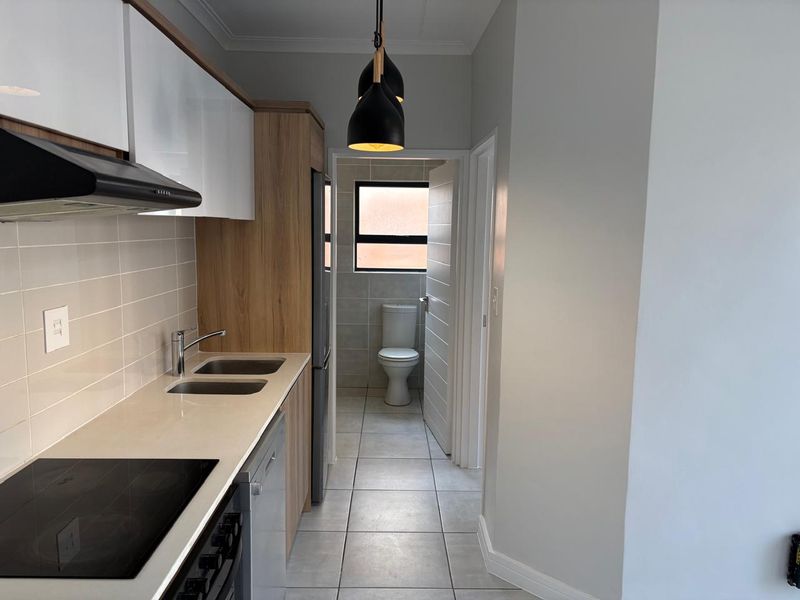 Modern kitchen featuring sleek cabinetry, electric hob, extractor fan, and tiled flooring, with an adjacent bathroom visible through the doorway.