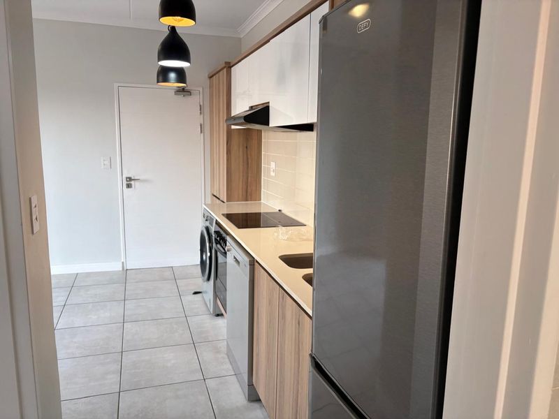 Modern kitchen featuring sleek wood-grain and white cabinetry, stone countertops, integrated electric hob, extractor fan, and stylish subway tile backsplash with tiled flooring.