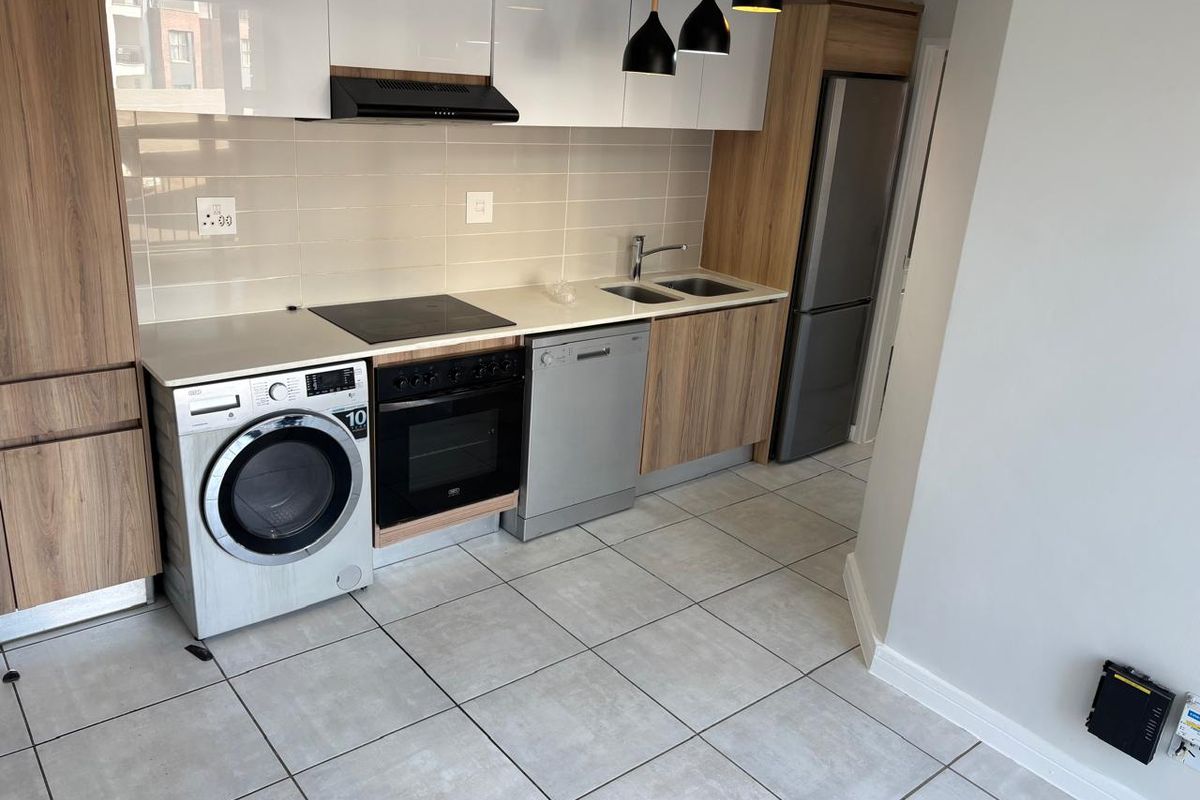 Modern kitchen featuring sleek white and wood-grain cabinetry, integrated appliances, tiled flooring, and a functional layout with ample storage and workspace.