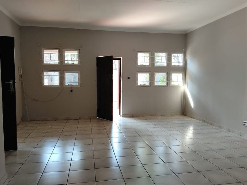 A spacious, empty living area featuring neutral wall paint, ceramic floor tiles, and multiple windows with security bars.