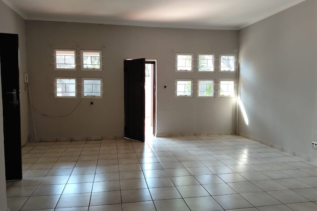A spacious, empty living area featuring neutral wall paint, ceramic floor tiles, and multiple windows with security bars.