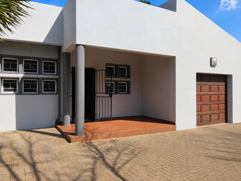 Front elevation of a modern house featuring a paved driveway, covered entrance porch with tiled flooring, and a wooden garage door.