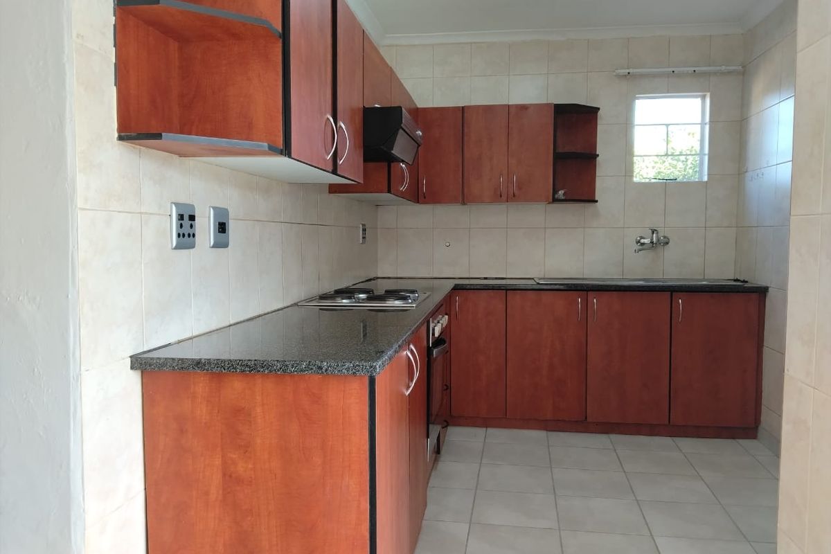 A functional kitchen featuring wood-finish cabinetry, granite countertops, a built-in hob and oven, and tiled finishes throughout.